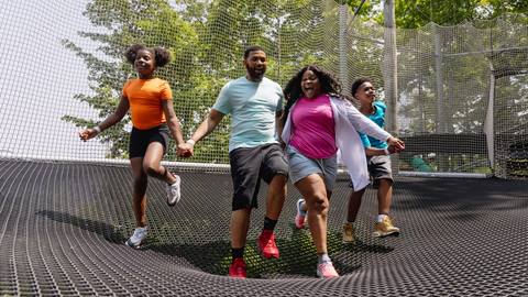 Four people happily jumping together on an outdoor trampoline.