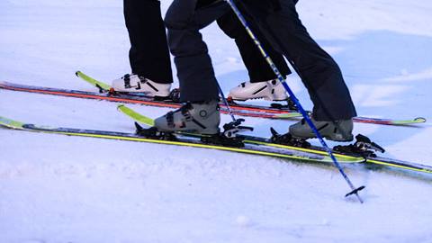 Two people skiing on snow, showing their skis, ski boots, and poles close-up.