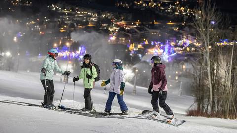 A group of skiers standing on a slope at night.