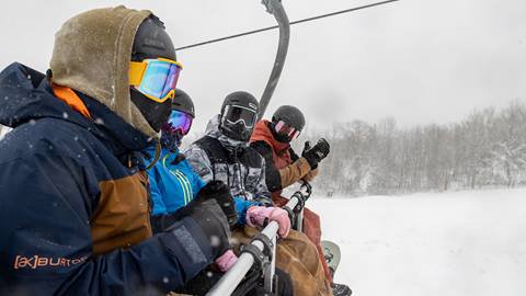 A group of people riding a ski lift in the snow.