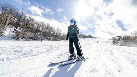 Person skiing down a snowy slope on a sunny day with a bright blue sky and a few scattered clouds in the background.