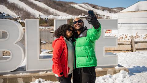 A couple taking a selfie in front of the Blue Sign at Blue Mountain Resort