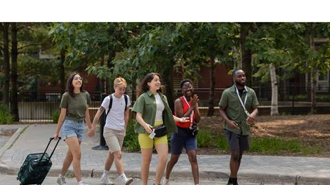 A group of students walking down a street with luggage.