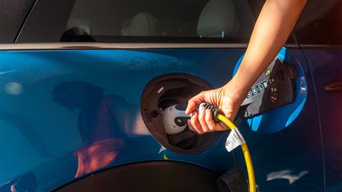 Hand plugging a charging cable into the port of a blue electric car.