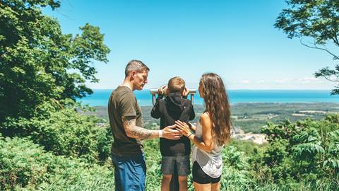 a family using binoculars to admire a panoramic view of a blue mountain beach from a forested hiking trail blue mountain resort
