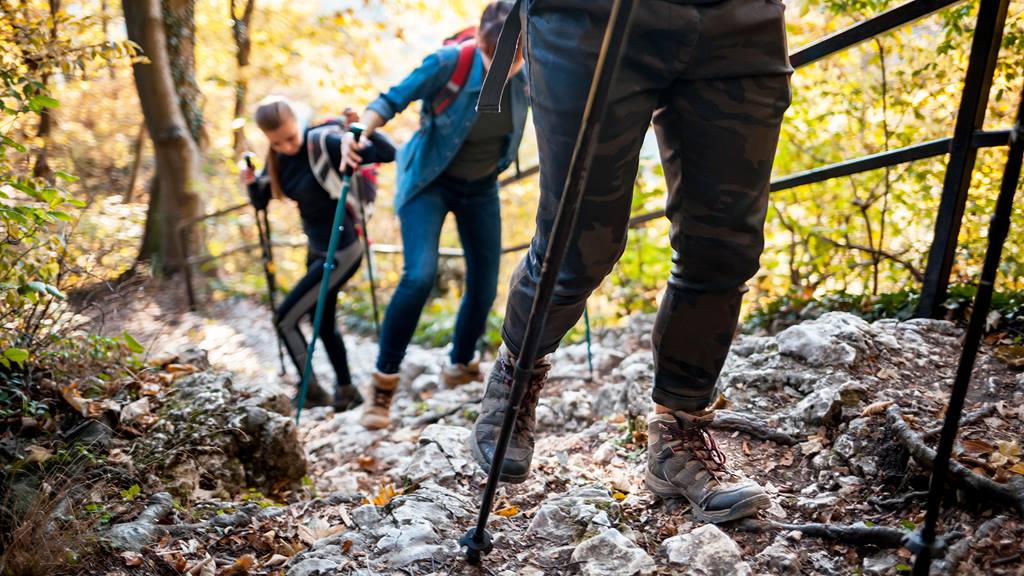 three people with trekking poles ascend a rocky hiking trail surrounded by autumn foliage at blue mountain resort