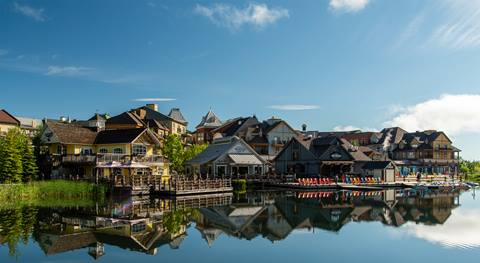 A picturesque waterfront view of buildings in various architectural styles under a clear blue sky, reflected in the calm water below.