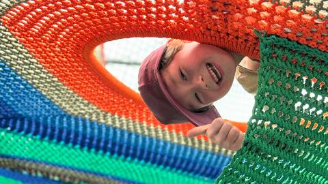 a boy on the cocoon crawl climbing net smiling and giving a thumbs up through an opening at blue mountain resort