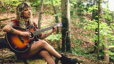 A woman playing guitar under a tree