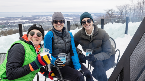 Three people sitting at a table on top of a snowy mountain.