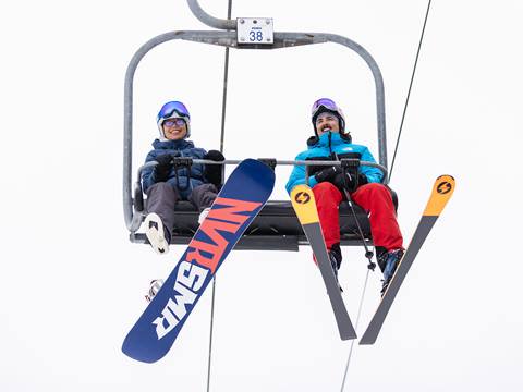 A skier and snowboarder riding up a chairlift