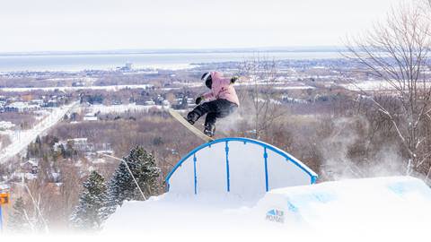 A snowboarder performs a trick on a blue rail with a snowy landscape in the background.