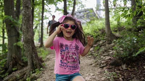 a child wearing heart-shaped sunglasses happily walking ahead of her family on a outdoor trail at blue mountain park