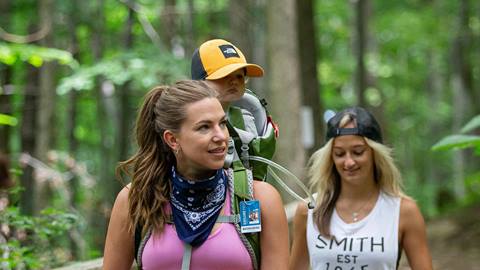 a blue mountain explore pass holder carrying a toddler in a carrier backpack with another adult hiking at blue mountain resort