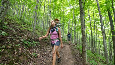 a person with a toddler strapped to their back leading another person through the trail at blue mountain resort