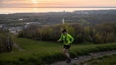 the sun rising above the blue mountain beach coast with a person running up a hiking trail at blue mountain resort